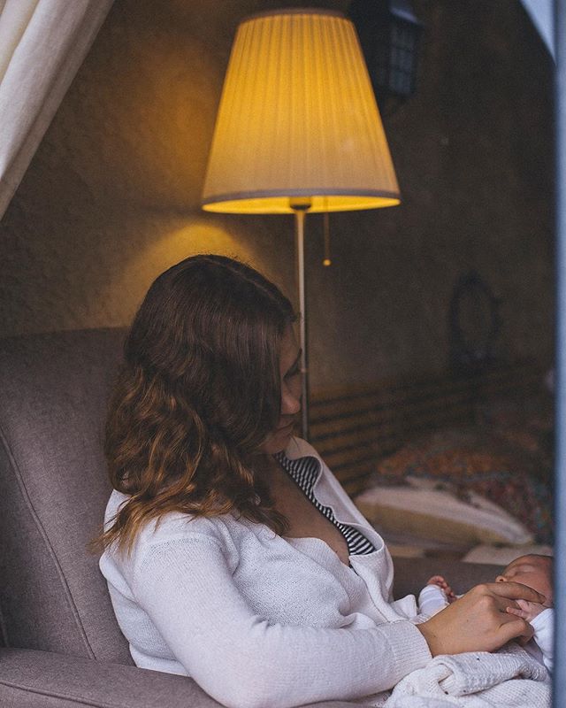 A mother is tenderly breastfeeding her newborn baby in a softly lit, intimate indoor setting.