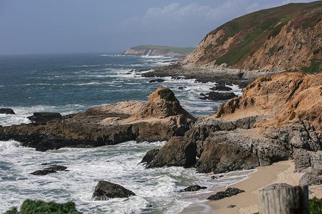 A scenic view of the California coastline featuring rocky cliffs, ocean waves, and a tranquil beach.