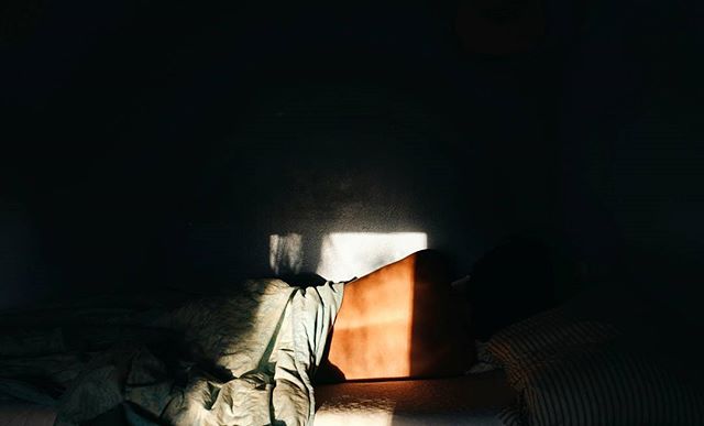 Person sleeping in a dimly lit bedroom with sunlight streaming through the window creating a peaceful and serene atmosphere.