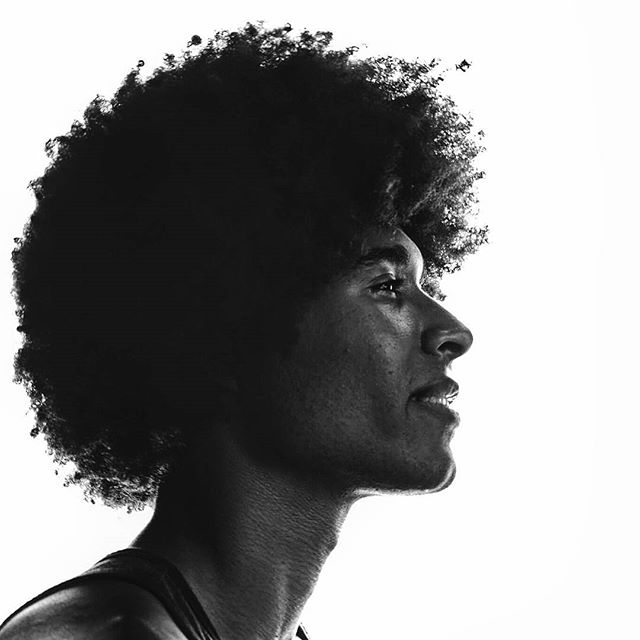 A black and white portrait of a man with afro hair in profile against a bright white backdrop, showcasing strength and confidence.