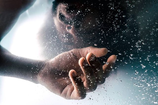 A close up view of a person's hand underwater, surrounded by water droplets, conveys a sense of mystery and emotion.