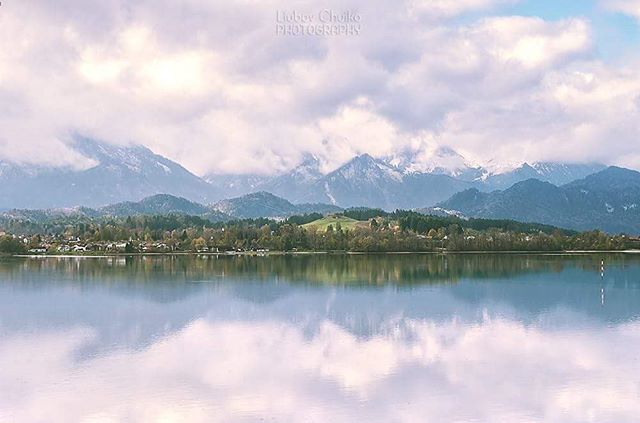 A tranquil lake reflects the cloudy sky and snow-capped mountains in this serene landscape photography.