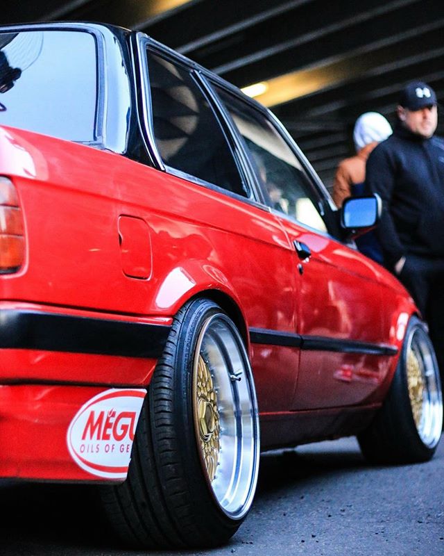 A red BMW E30 with custom wheels and Meguiars sticker on the street.