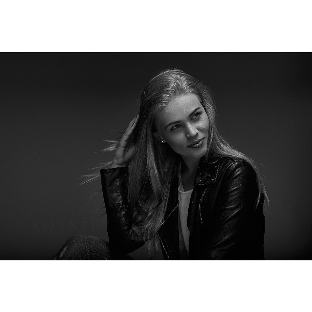 Black and white portrait of a blond woman in a leather jacket posing in studio.