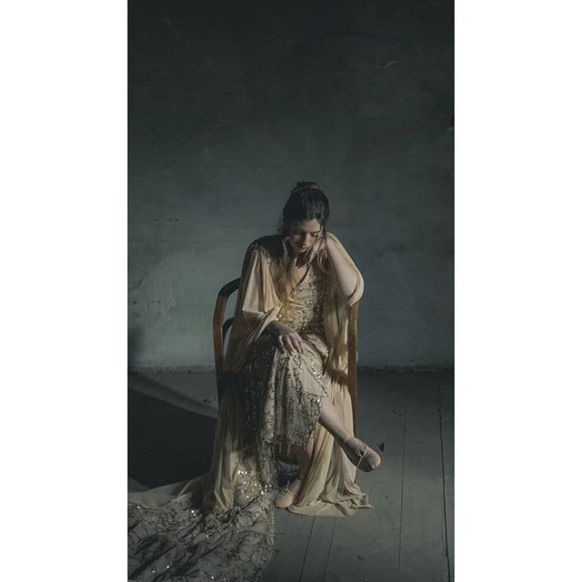 A woman in a vintage dress sits thoughtfully in a dimly lit room.