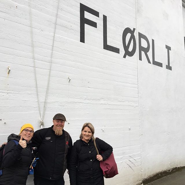 Three people standing in front of a white wall with black lettering that says "FLØRLI".