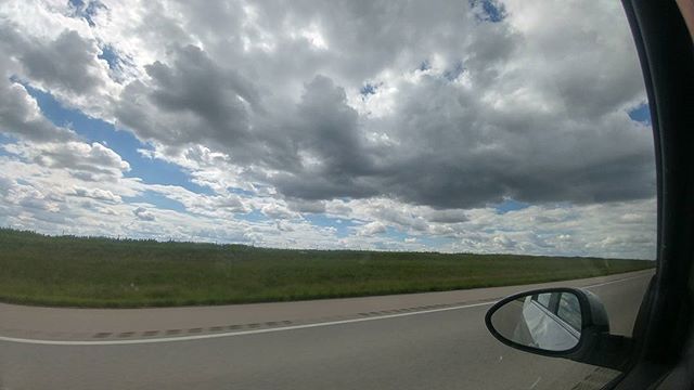 A scenic road stretches into the distance under a cloudy sky, captured from inside a moving vehicle.