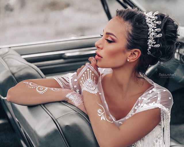 A beautiful bride with henna art poses elegantly in a car, exuding dreamy sophistication.