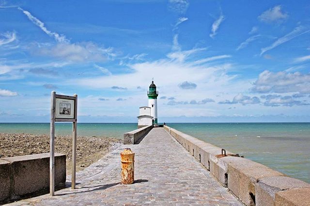 Scenic view of a lighthouse at the end of a pier on a sunny day, perfect for travel and tourism campaigns.