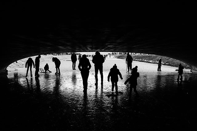 Silhouettes of people ice skating under a tunnel on a frozen winter day, creating a dynamic scene.