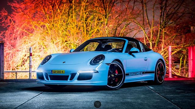 A sleek light blue Porsche Targa stands out in the night with an appealing glow.