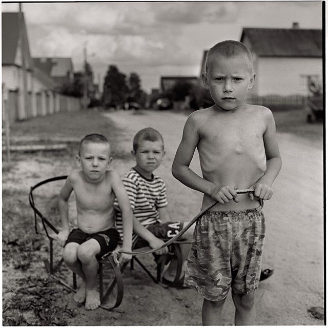 Three young boys pose in a black and white image on a rural street, conveying a sense of childhood and community.