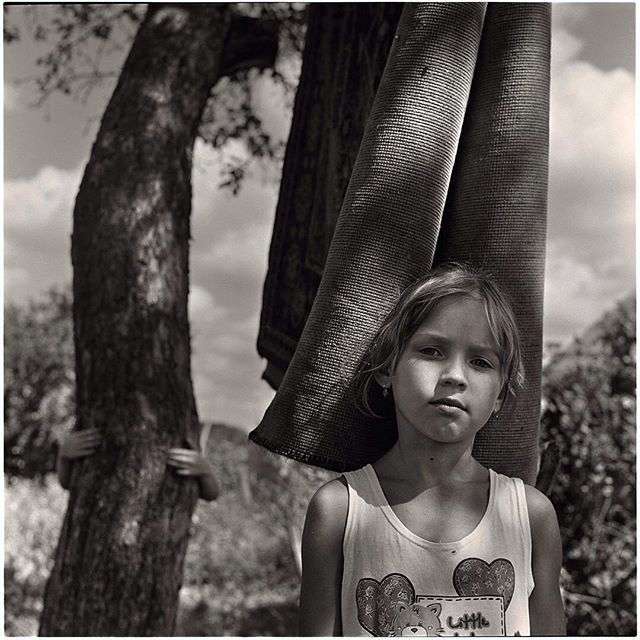 A young girl stands outside with a rug over her shoulder in a black and white shot.