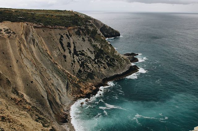 A scenic view of a rugged coastline with towering cliffs meeting the deep blue ocean under a cloudy sky.