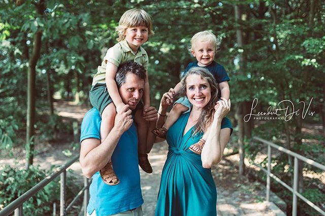 A happy family with two young sons on their parents' shoulders poses for a photo in a park. 