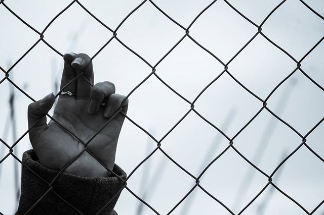 A close-up in black and white shows a hand gripping a wire fence, conveying a sense of restriction or hope.
