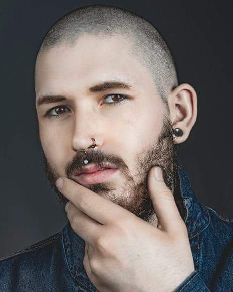 Portrait of a man with piercings and a beard in a studio setting.  