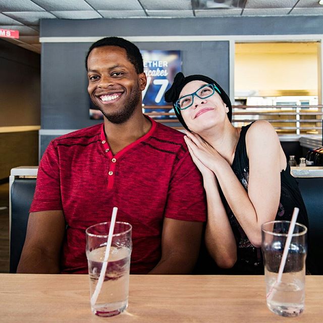 A happy couple smiles at a diner, enjoying drinks at a table.