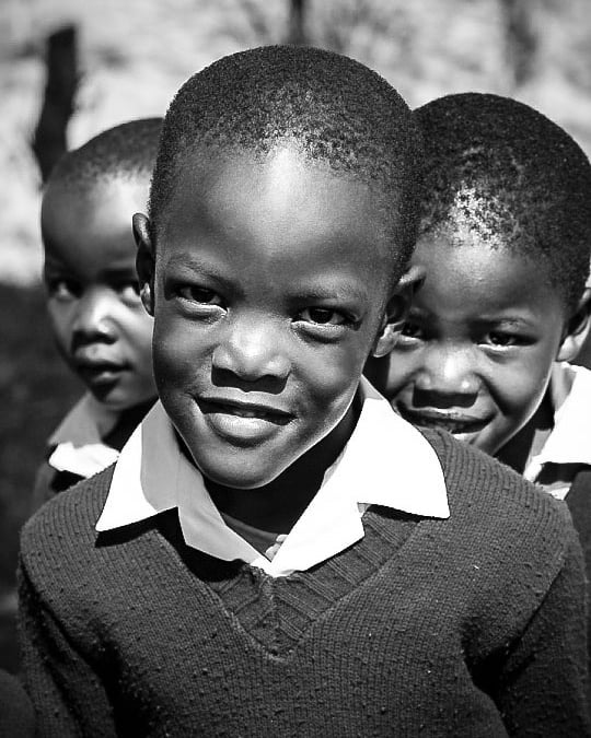 Three smiling schoolboys in black and white, wearing uniforms, outdoors.