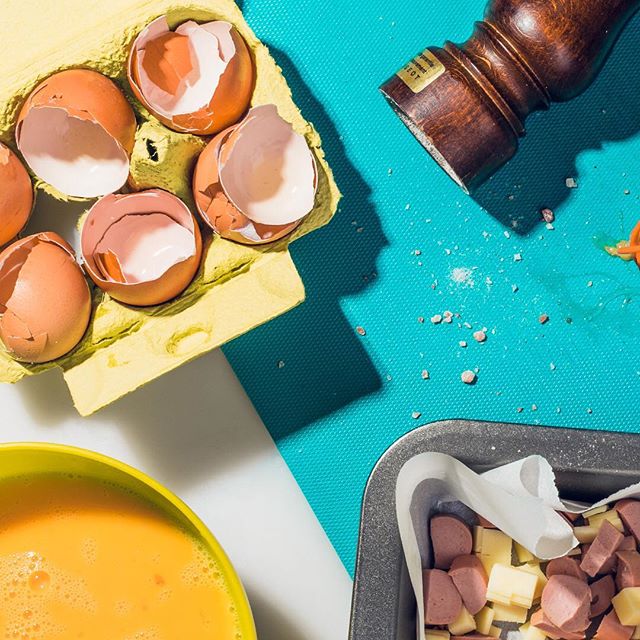 Overhead shot of scrambled eggs, cheese, meat, and seasonings in a kitchen setting.
