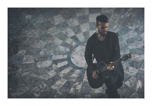 A man plays guitar with a soulful expression in a modern studio.