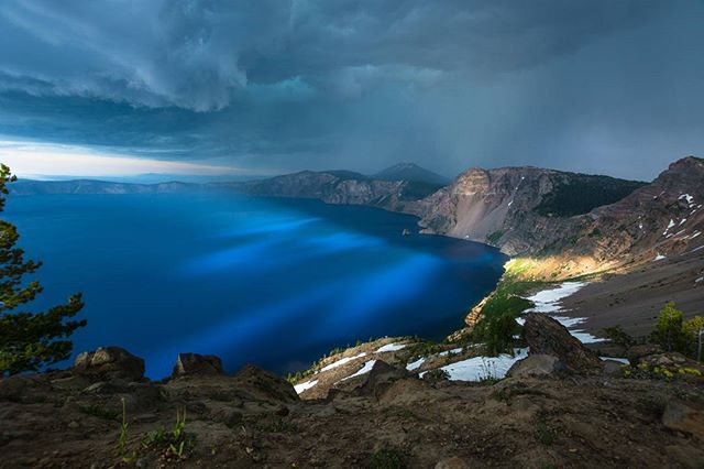 Dramatic view of Crater Lake's blue waters surrounded by mountains under a stormy sky.