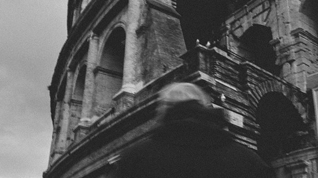 A black and white low-angle view of the Colosseum in Rome, Italy, capturing its ancient and weathered architecture.