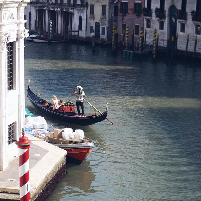 A gondolier rows tourists in a gondola on a canal in Venice, Italy, with buildings in the background.