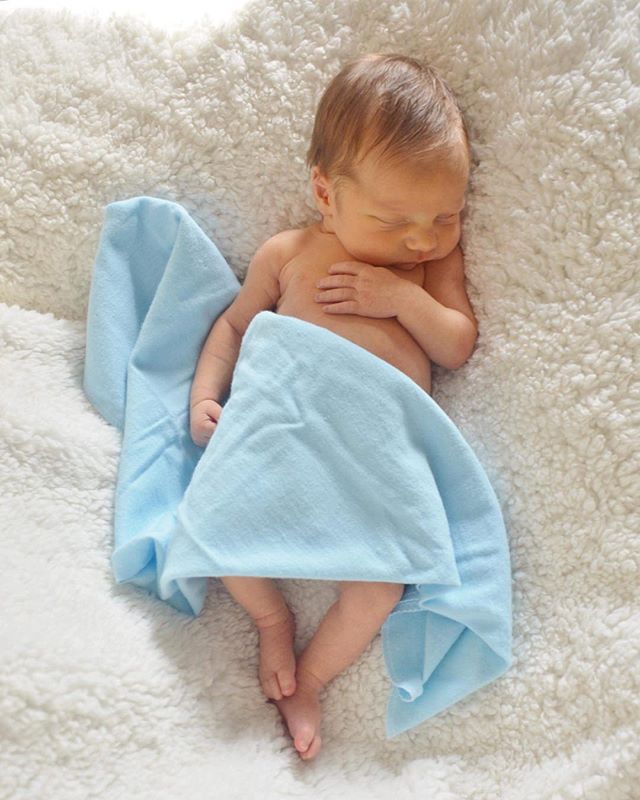 A newborn baby sleeps peacefully wrapped in a light blue blanket on a soft, white surface.
