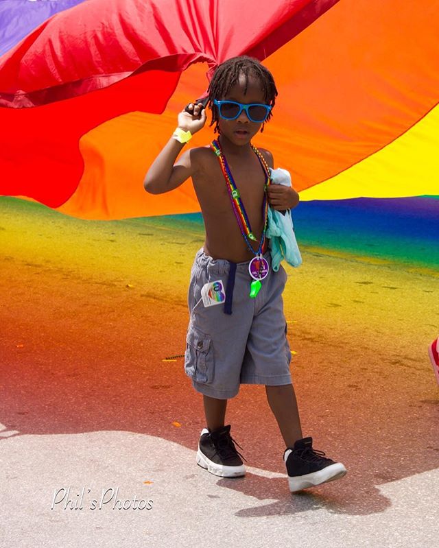 A young boy in sunglasses celebrates Pride with a rainbow backdrop, creating a vibrant and joyful image.