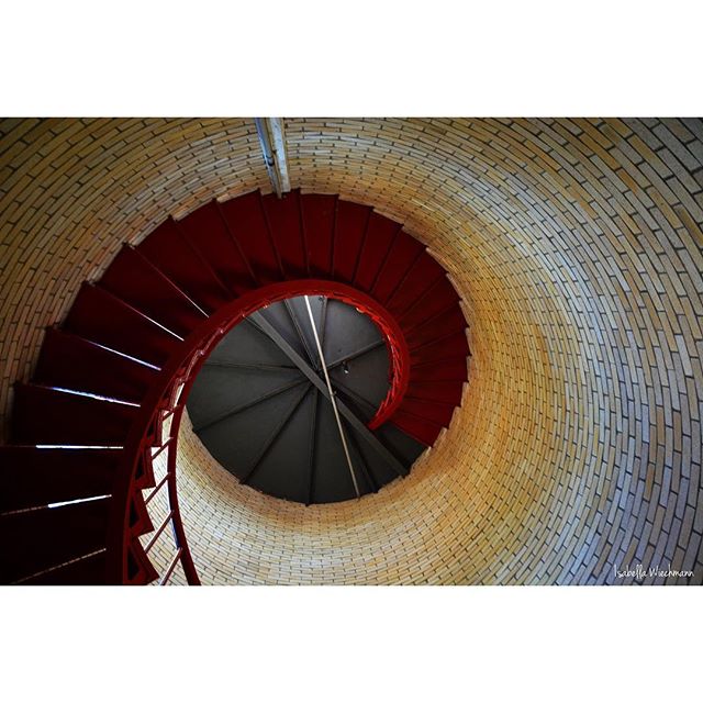 A striking high angle shot reveals a red spiral staircase within a brick tower, creating a captivating architectural composition.