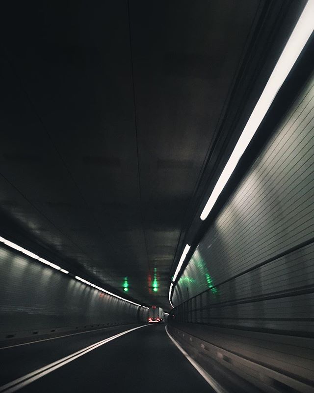A perspective view looking through a dark tunnel illuminated by overhead lights and road markings.