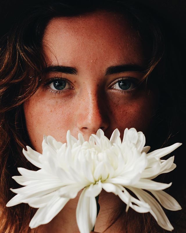 A woman's face is partially obscured by a white flower in a dreamy, intimate portrait.
