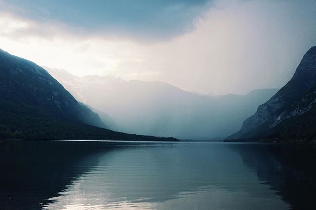 A tranquil lake is surrounded by majestic mountains under a cloudy sky, a serene nature scene.