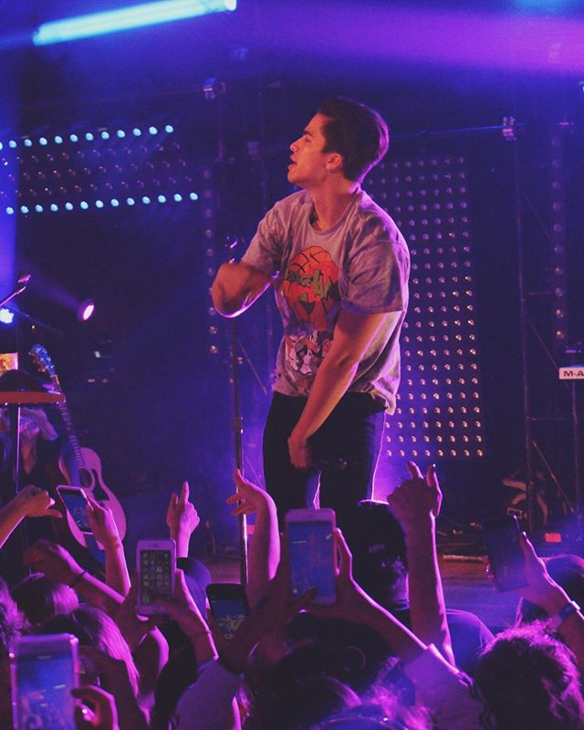 A performer sings on stage at a concert with an enthusiastic audience recording the show.