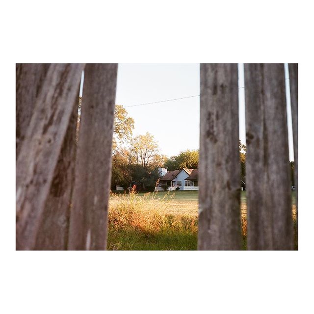 A quaint house is glimpsed through a rustic wooden fence, evoking a sense of tranquility and simple rural living.