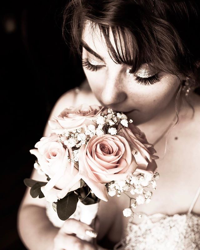 A woman in sepia tones softly smells a bouquet of pink roses and baby's breath flowers.