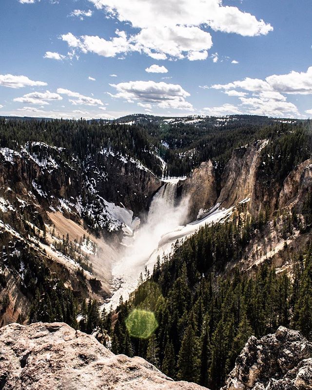 A breathtaking view of a powerful waterfall cascading down a rocky canyon surrounded by lush green trees and mountain landscape.