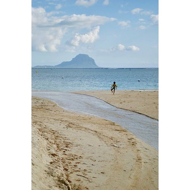 A boy runs on a sandy beach near the ocean on a sunny day.