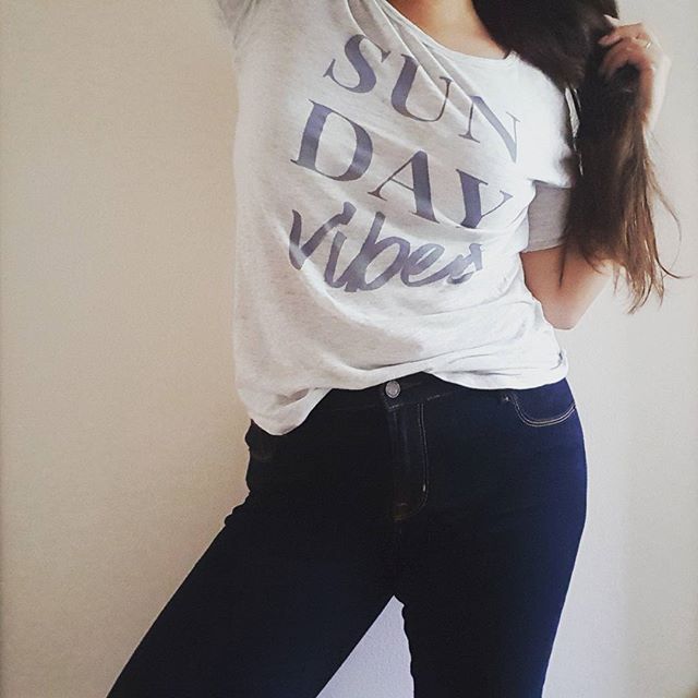 A woman poses in a casual outfit consisting of a t-shirt and jeans.