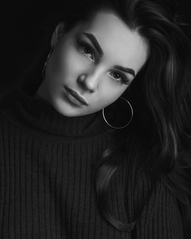 A monochrome portrait of a woman with hoop earrings, captured in a studio setting with soft lighting.