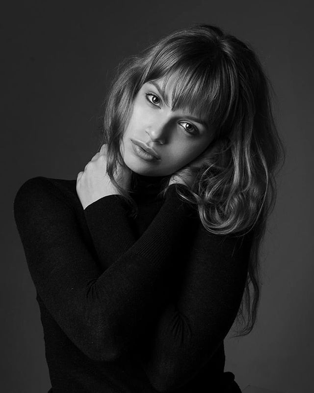 A black and white portrait of a young woman with bangs in a studio setting, exuding calm and intimacy.