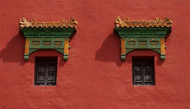 Ornate windows adorn a traditional red wall, highlighting the beauty of architectural heritage and design.