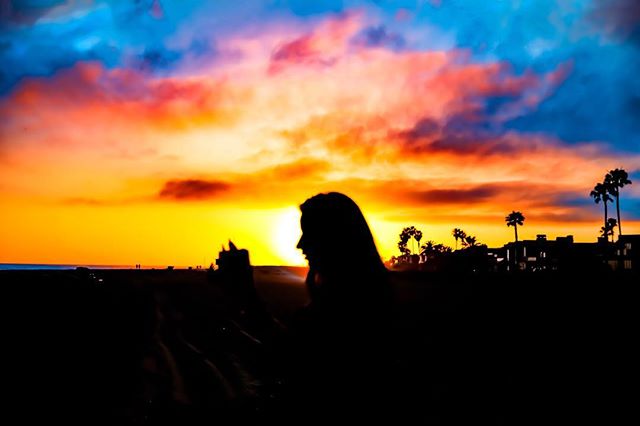 Silhouette of a woman against a vibrant sunset at the beach with palm trees. 