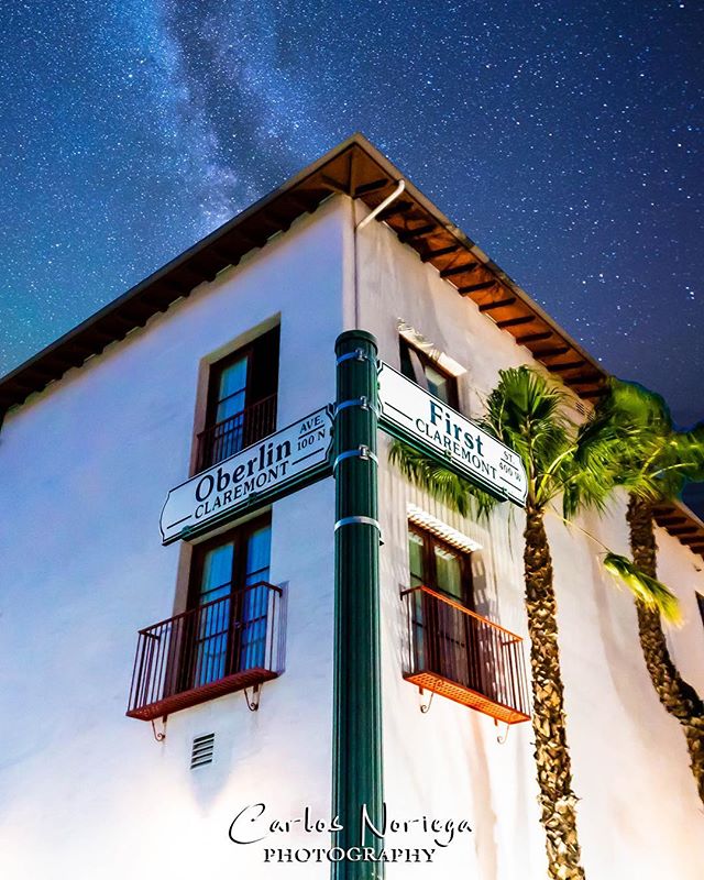 Night view of the corner of a building with palm trees and street signs in Claremont, California under a starry sky.