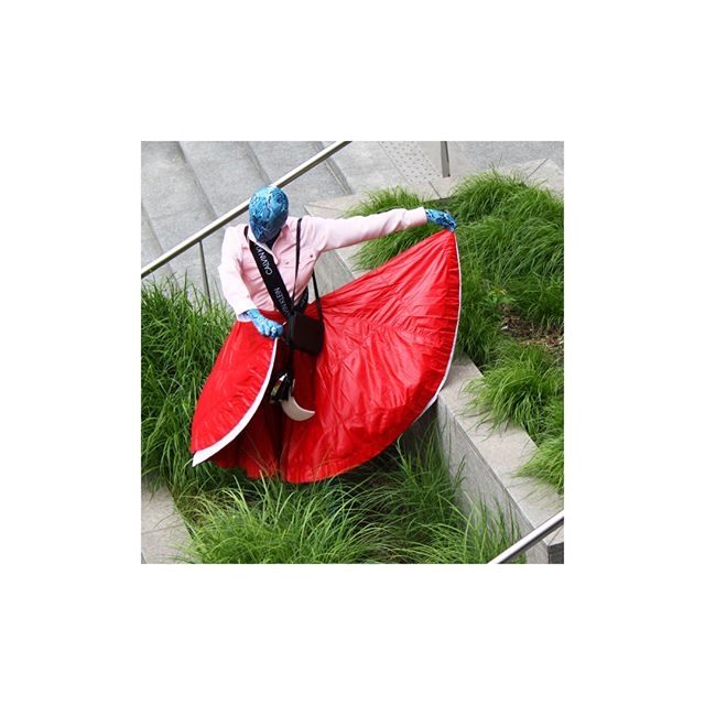 A person in a red skirt poses playfully on steps surrounded by lush grass. 