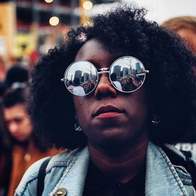 A woman with sunglasses reflects a cityscape during a protest in this editorial-style portrait.