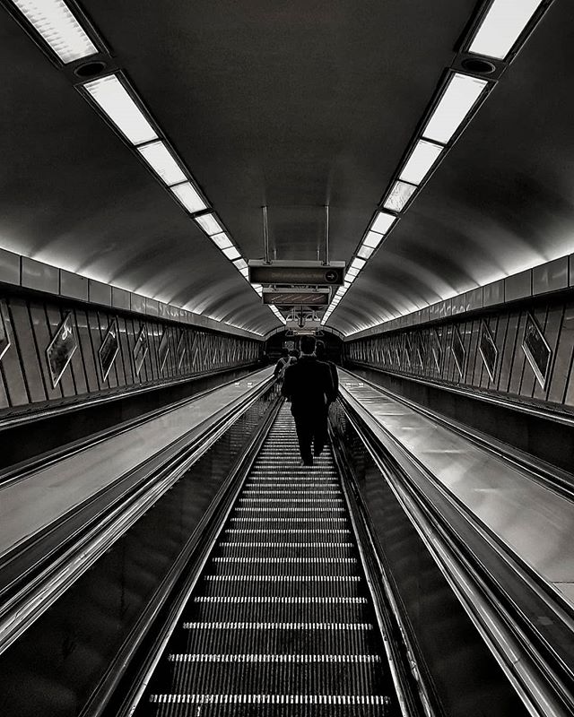 A man walks down an escalator in a monochrome tunnel, showcasing urban commuting and public transportation.