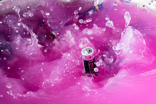 An AA battery is immersed in vibrant pink liquid, creating a dynamic splash.