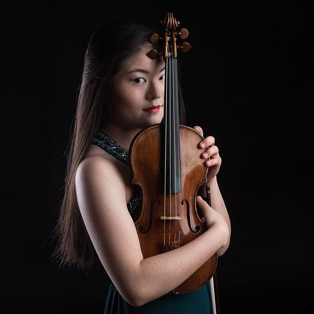 Portrait of a young woman holding a violin in a studio with a dark background.
